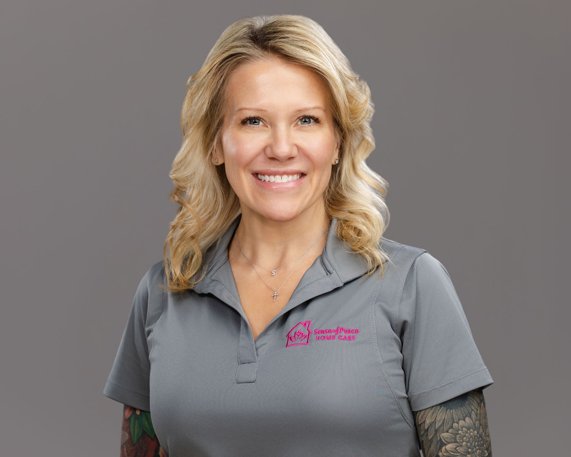 A woman is wearing a gray shirt and smiling for the camera.