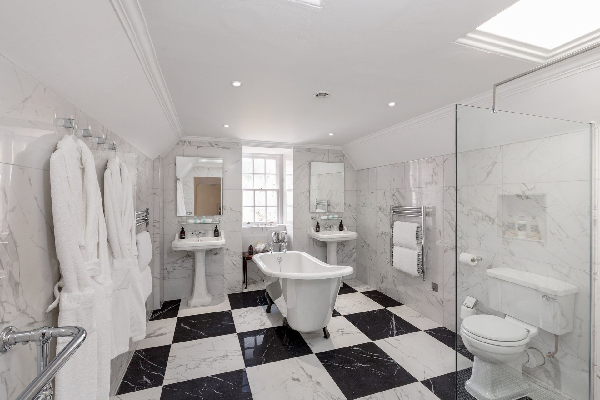 A bathroom with a bathtub, toilet, sinks and a checkered floor.