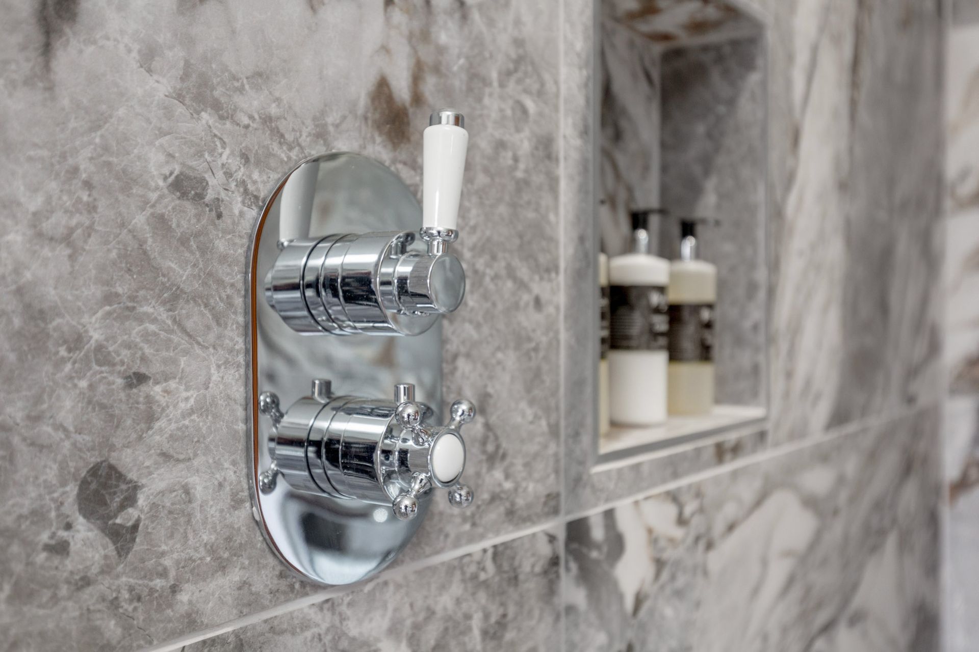 A close up of a shower head on a marble wall in a bathroom.