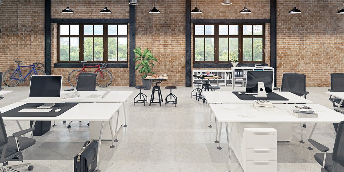 An empty office with white desks and chairs and a brick wall.