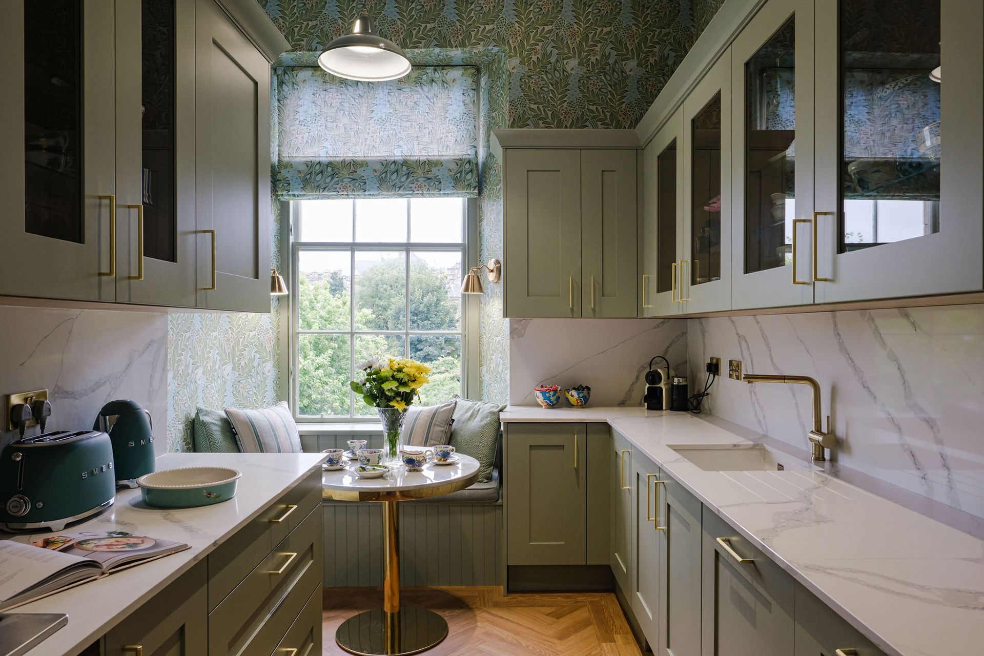 Sage green kitchen with marble countertops, window nook and small round table.