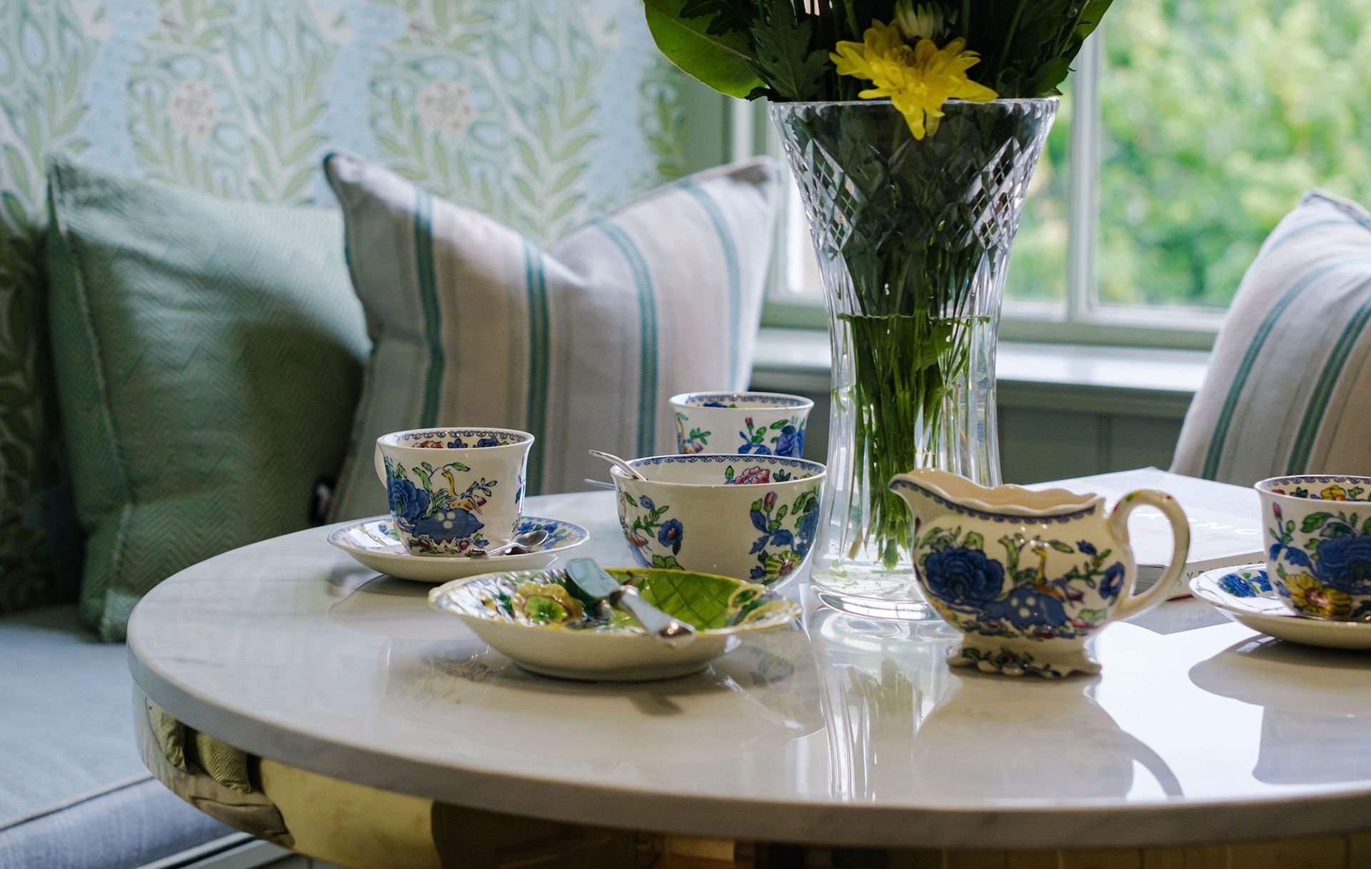Table setting: blue floral teacups, bowls, and creamer; flowers in vase.