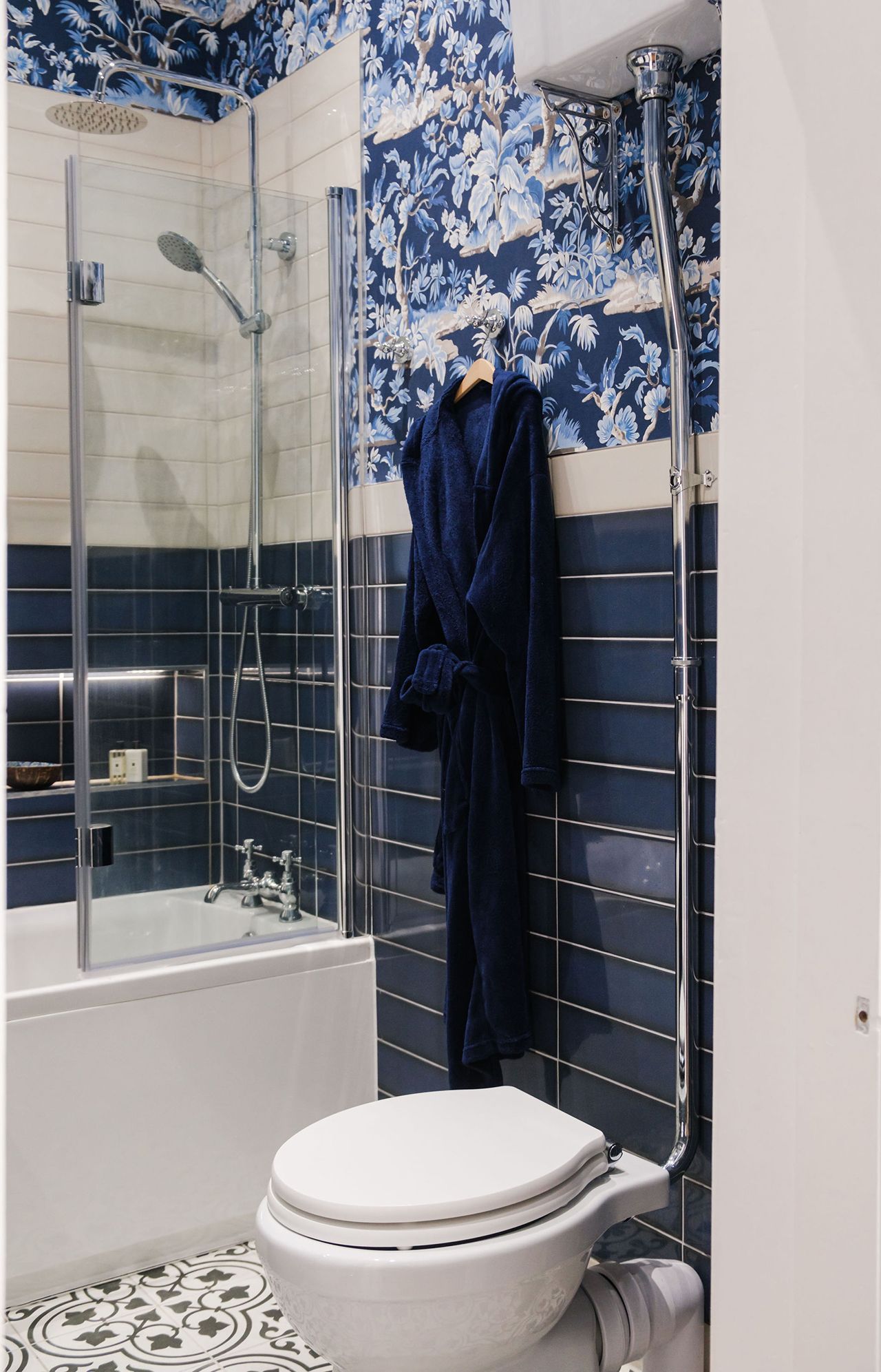 Blue and white tiled bathroom with a shower, toilet and robe hanging on the wall.