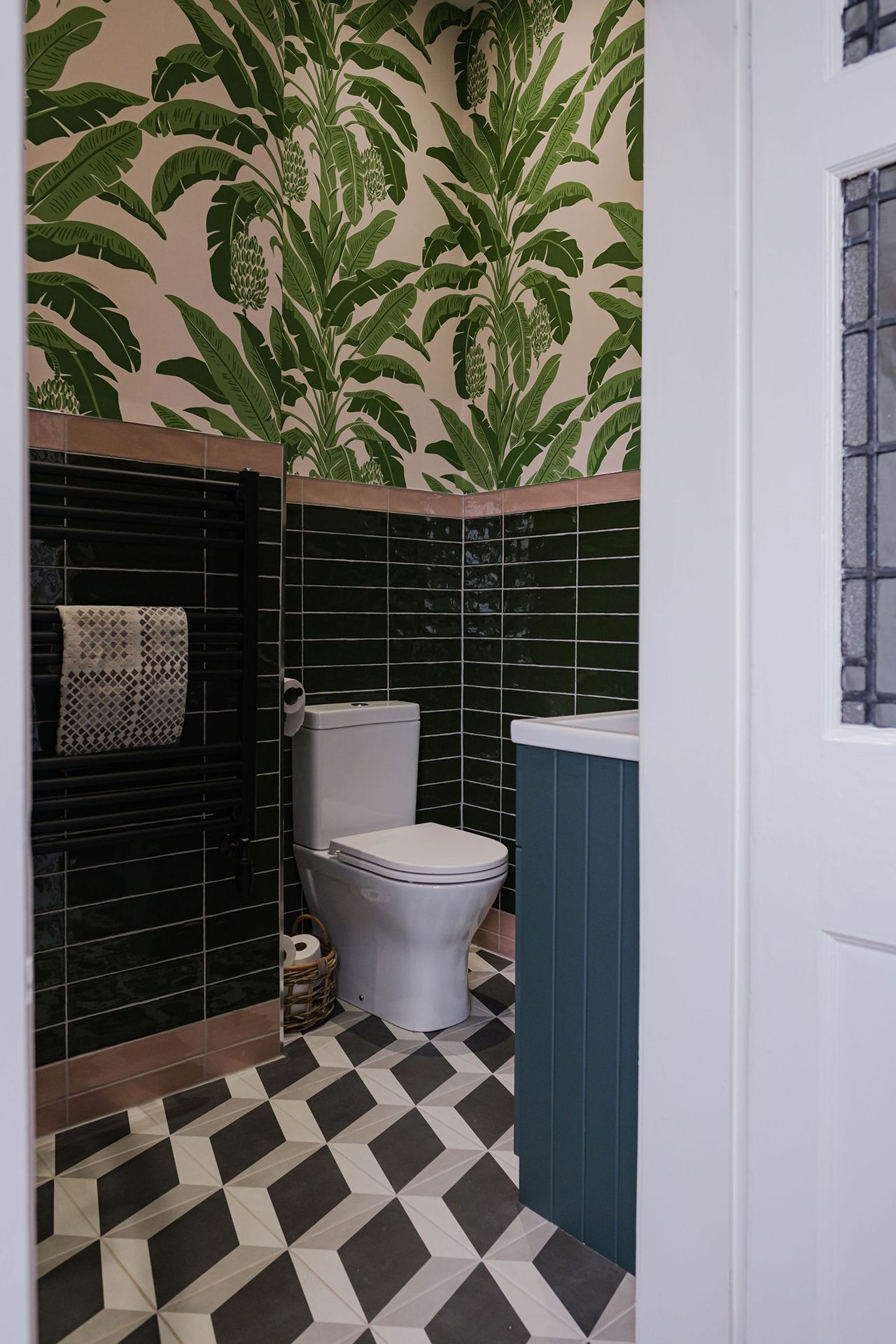 A bathroom with green and pink tropical wallpaper, dark green tiles and a patterned floor.