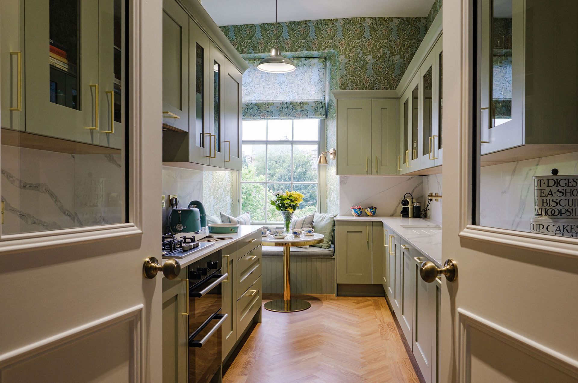 Green kitchen with cabinets, oven and a small table by a window.