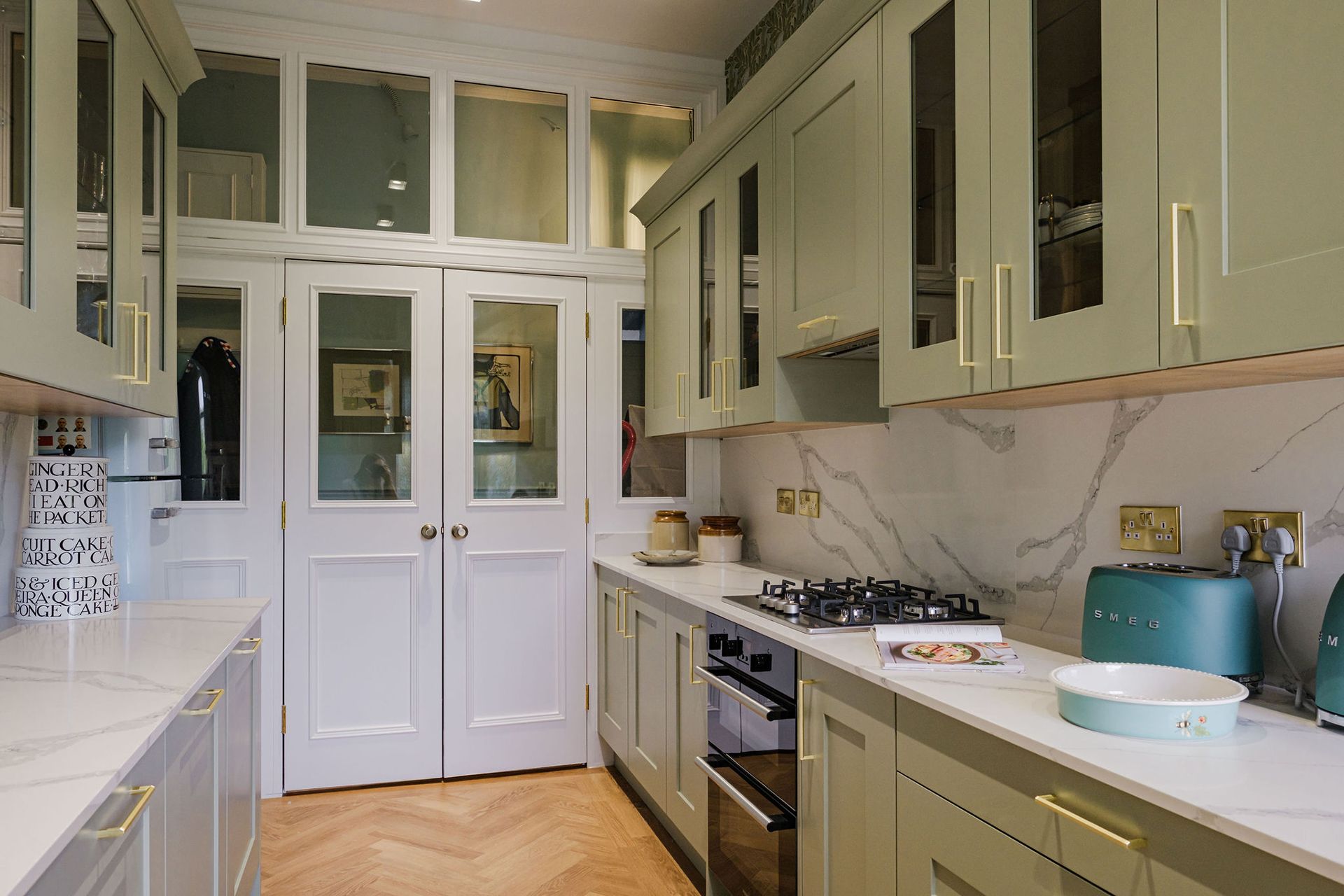 Green and white kitchen with cabinets, marble countertop and glass doors.