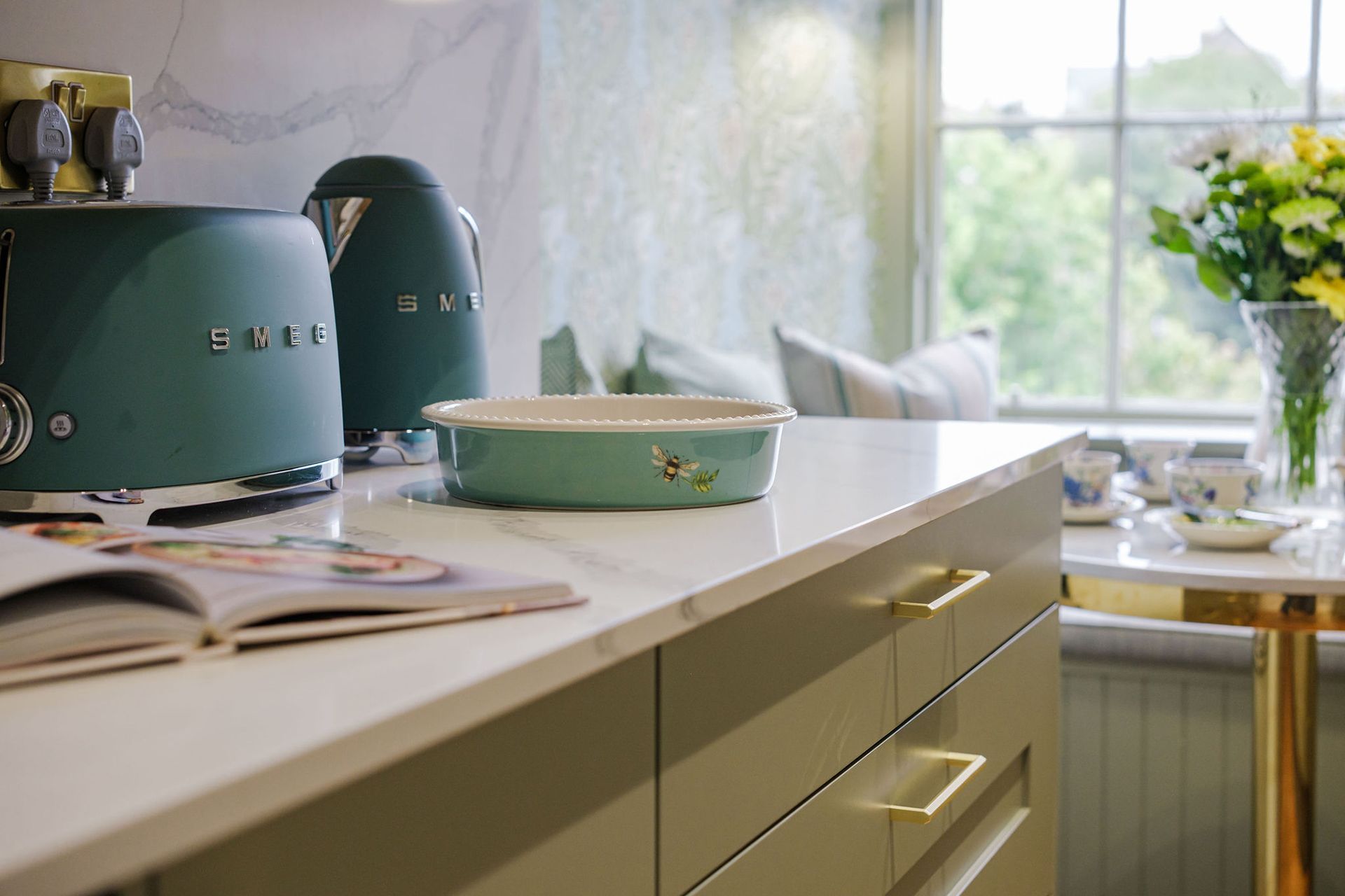 Teal toaster, kettle, and bowl on kitchen counter. Sunlight streams through a window.