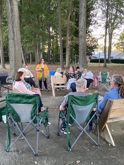 A group of people are sitting in folding chairs around a fire pit.