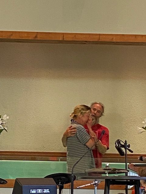 A man and a woman are hugging in front of a microphone in a room.