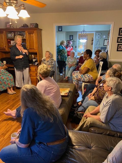 A group of people are sitting in a living room listening to a woman speak