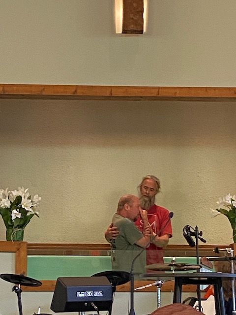 Two men are hugging in front of a microphone in a church.