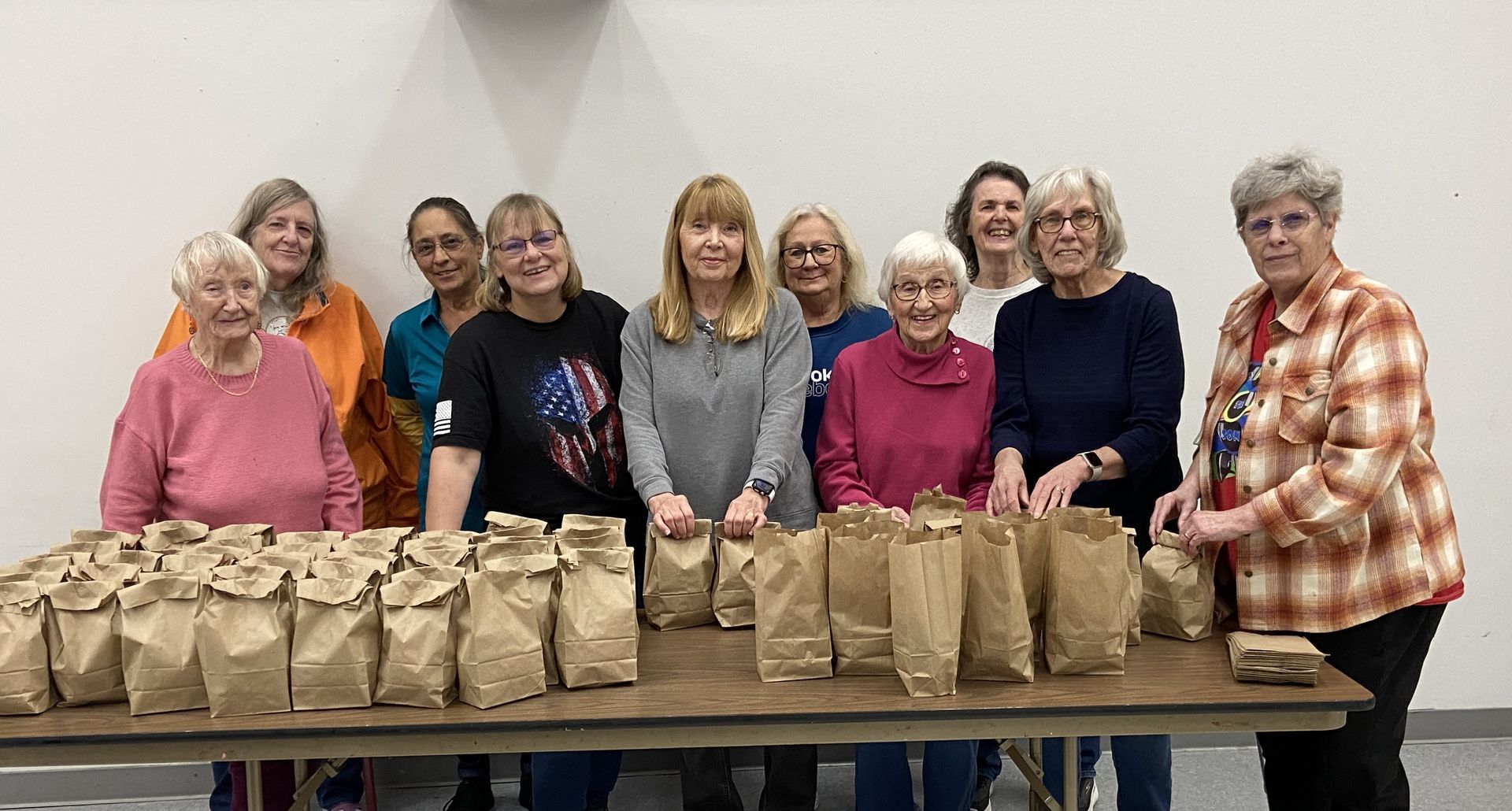 A group of women are standing around a table with bags of food.