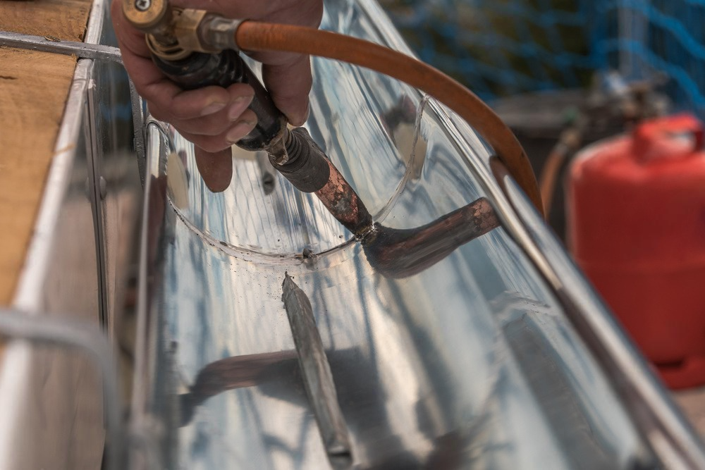 a person is welding a metal gutter with a torch .