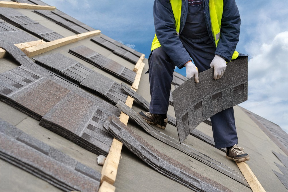 a man is kneeling on a roof holding a piece of shingles .