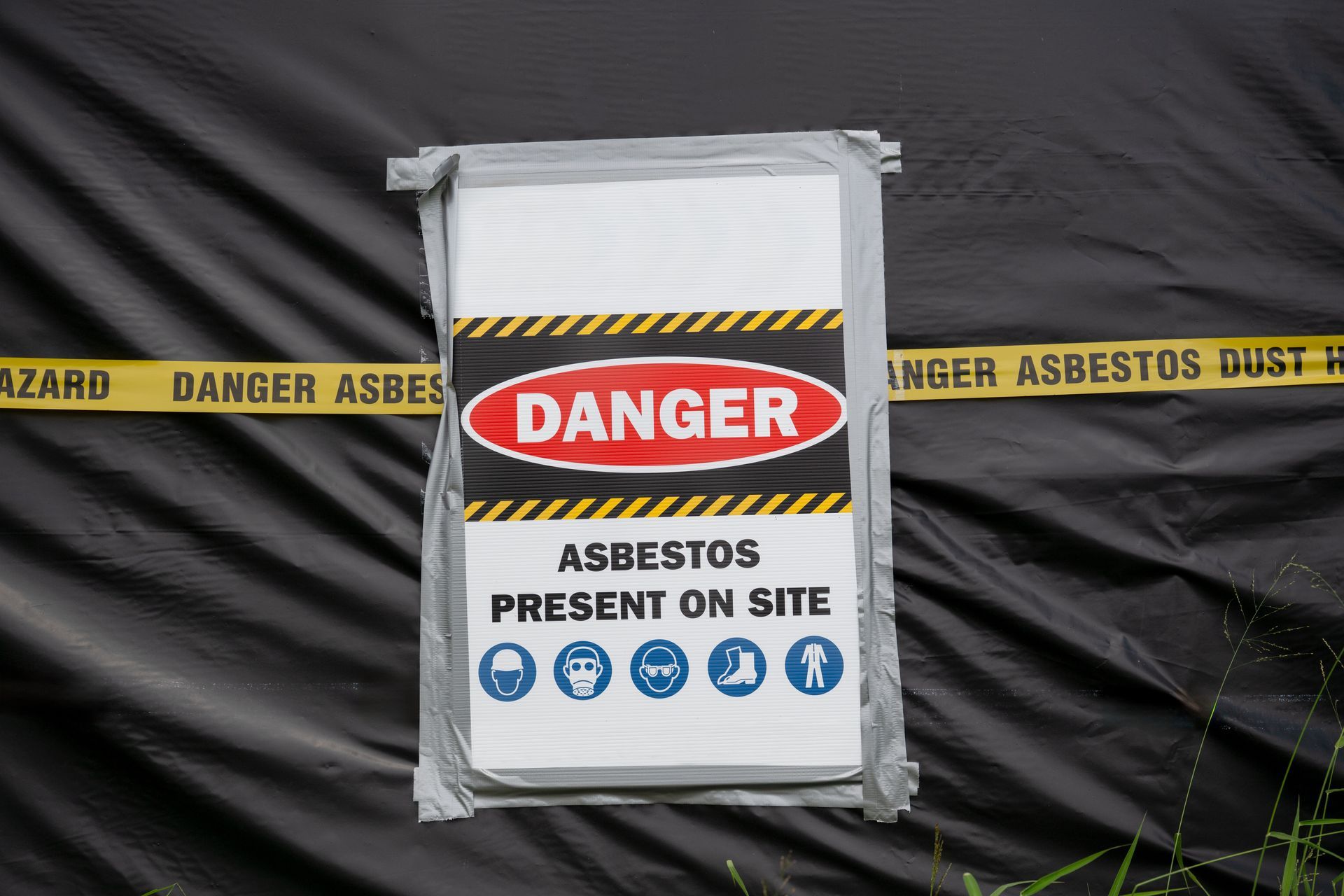 An asbestos danger hazard sign with a yellow ribbon in front of a black tarp.