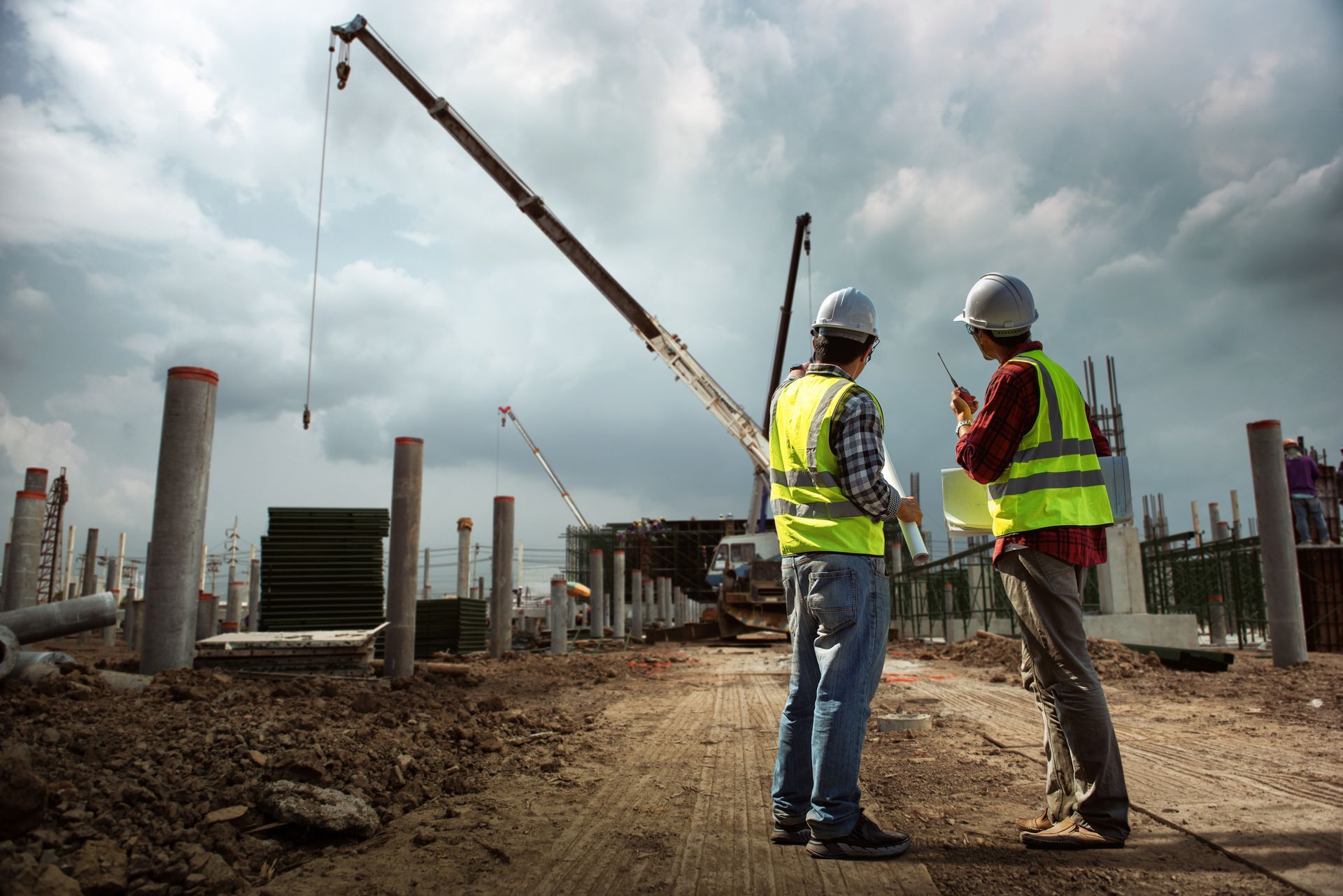 Two construction engineers are seeing a demolition crane from afar, in a demolition site.