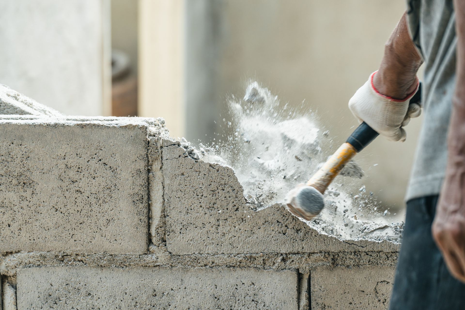 Close-up of a hand of a worker using a hammer to smash and demolish a brick block wall.