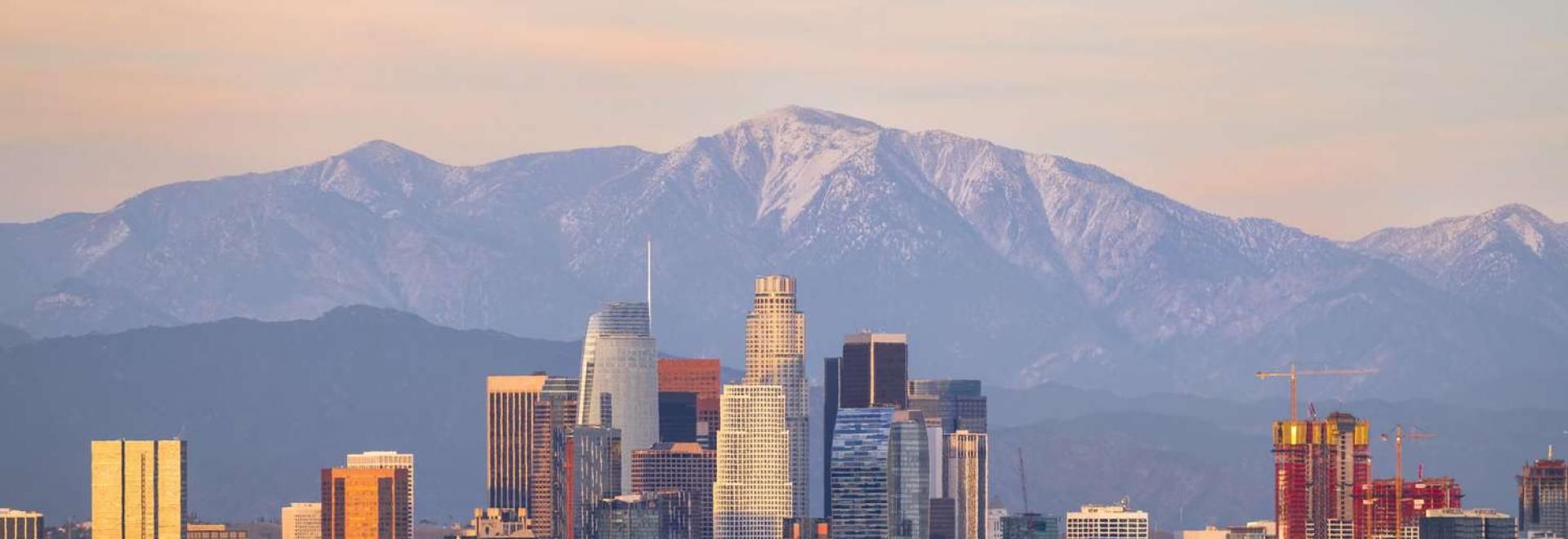Los Angeles skyline with snow-capped mountains in the background under a pastel sky.