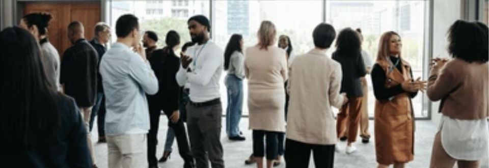 Group of diverse professionals in a modern office setting, conversing and clapping near large windows.