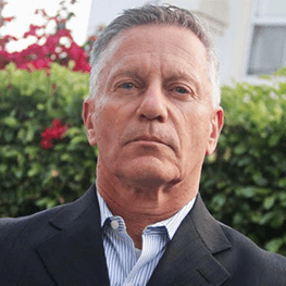 Older man, suit jacket, looking directly at the camera, neutral expression, outdoors.