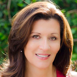 Woman with brown hair smiles at the camera; outdoor setting, green background.
