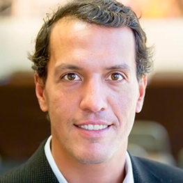 Man with brown eyes, smiling, wearing a black blazer and white shirt.
