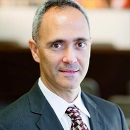 Man in suit, smiling, dark hair, light skin, indoor setting, business attire.