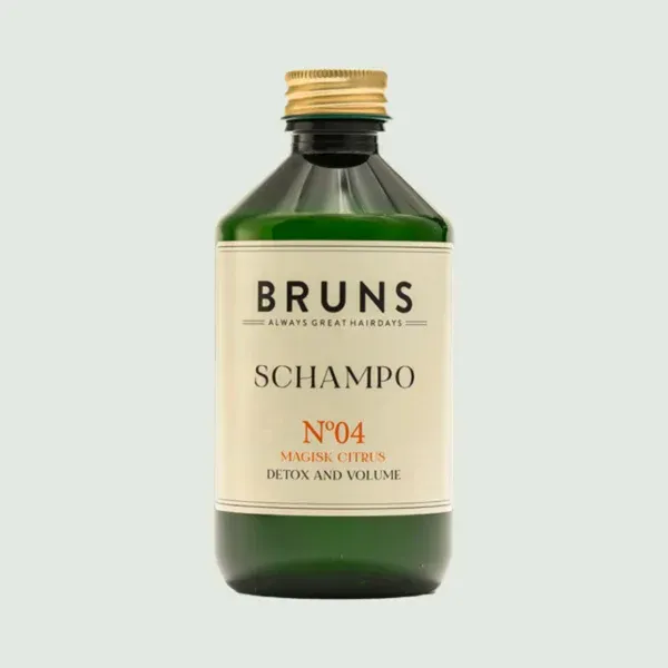 Een groene fles Bruns No. 04 Magisk Citrus shampoo met een gouden dop en een crèmekleurig etiket op een lichtgrijze achtergrond.