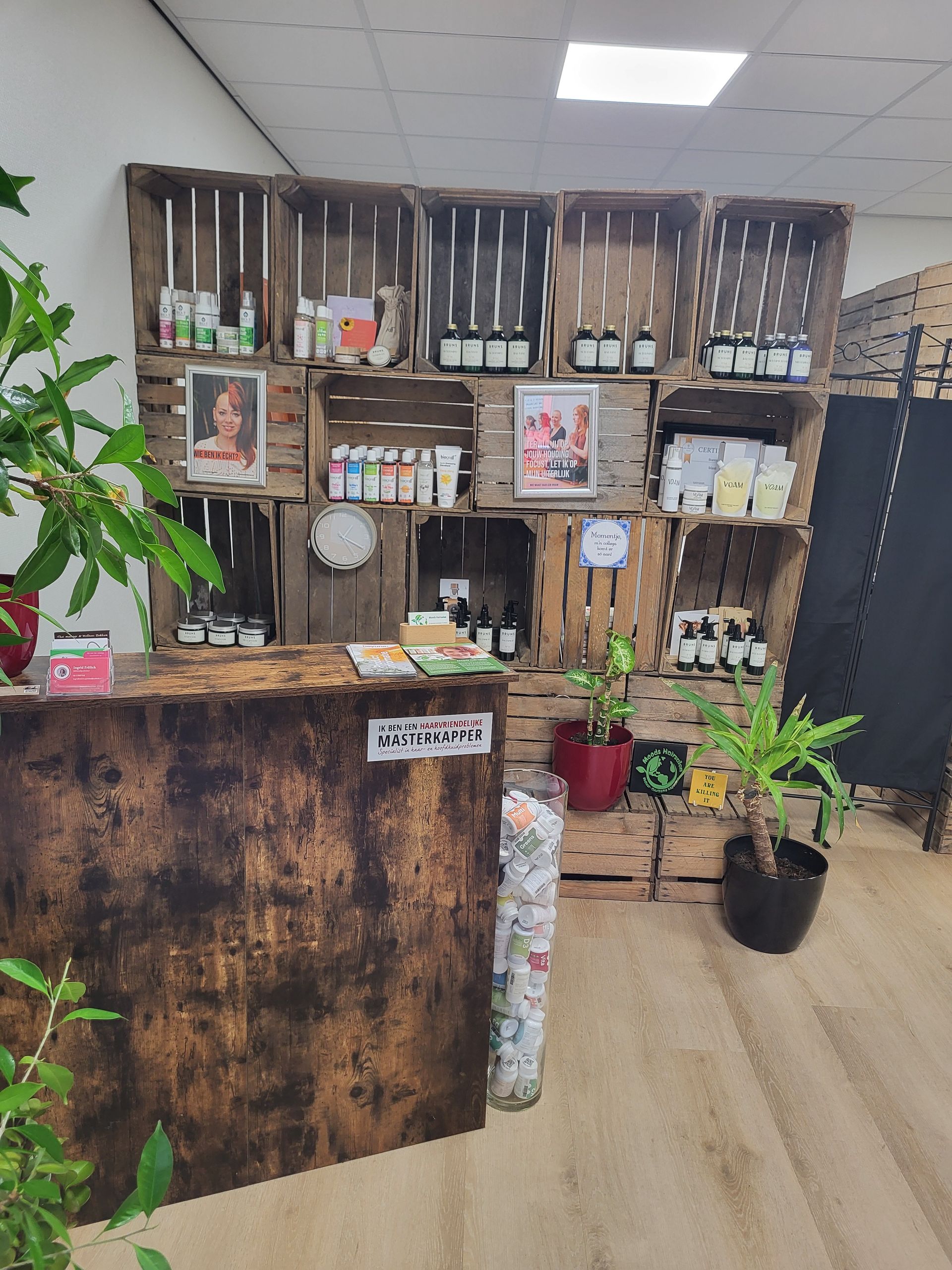 Een rustieke toonbank met houten lambrisering voor een stellingkast van gestapelde houten kratten waarop diverse winkelproducten worden tentoongesteld.