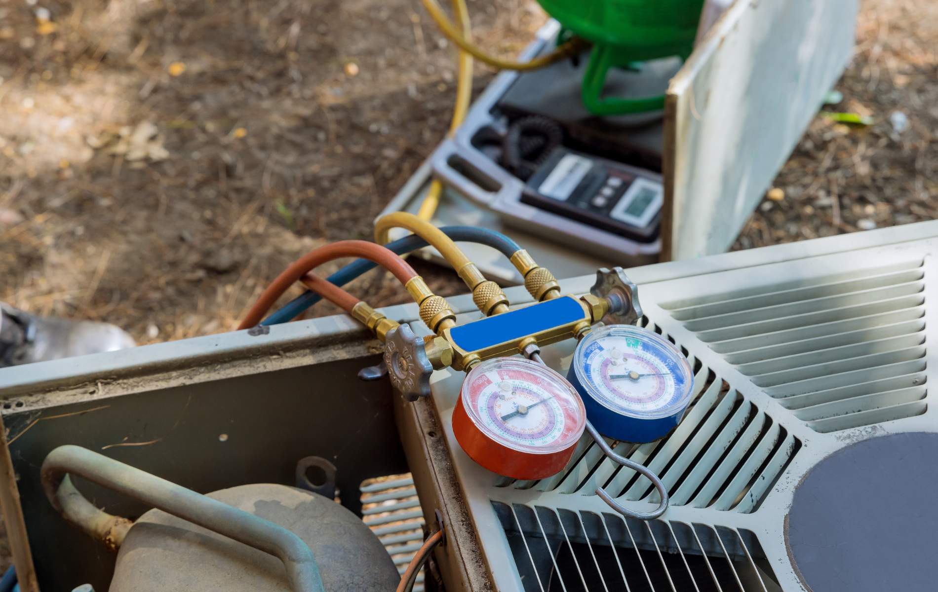 A close up of an air conditioner being repaired with gauges attached to it.