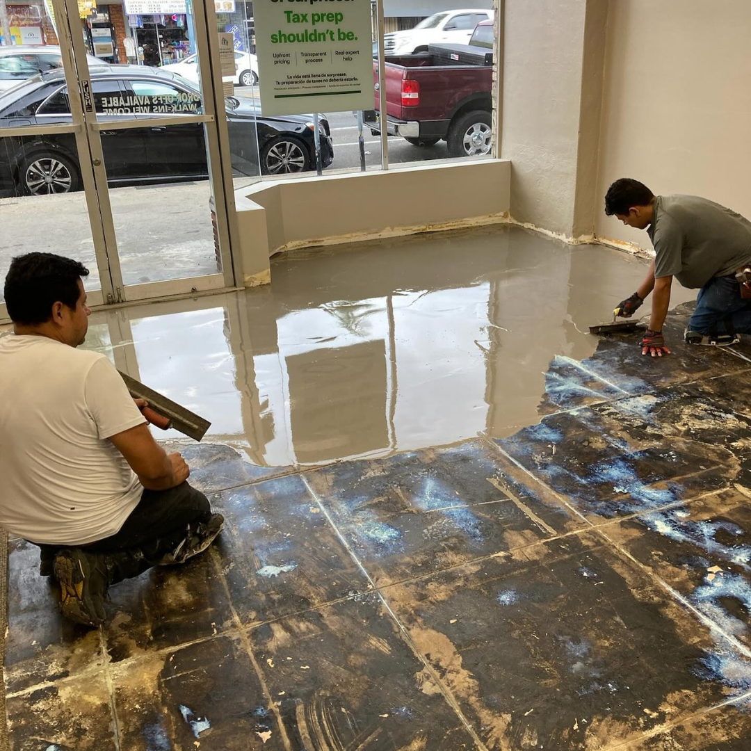 Two people installing carpet in a room, kneeling and working near the walls.