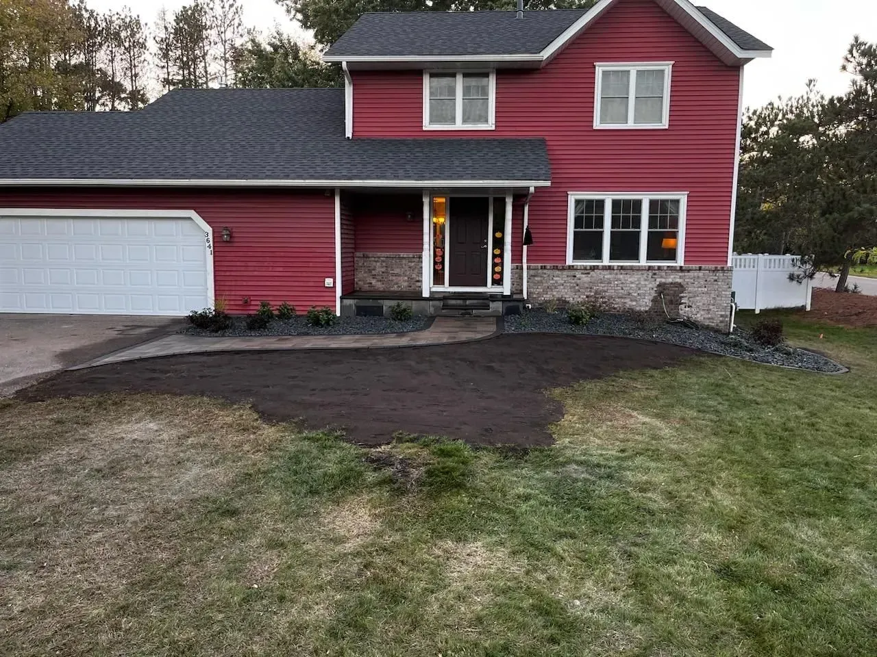 Red two-story house with a white garage door. Dark mulch and landscaping surround the front entrance. Grassy lawn.