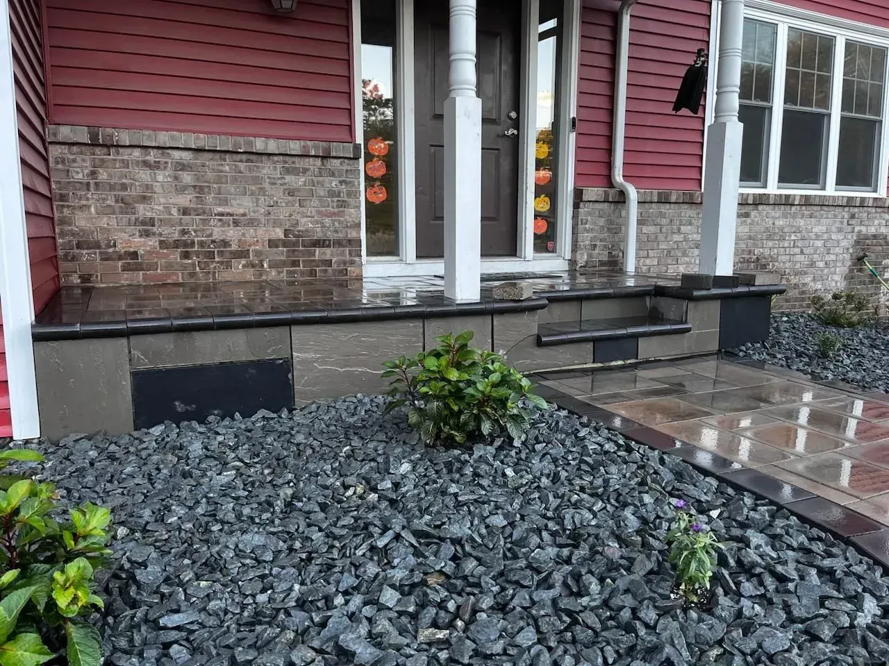 Front porch with stone steps and a walkway, bordered by dark gray landscaping rocks.