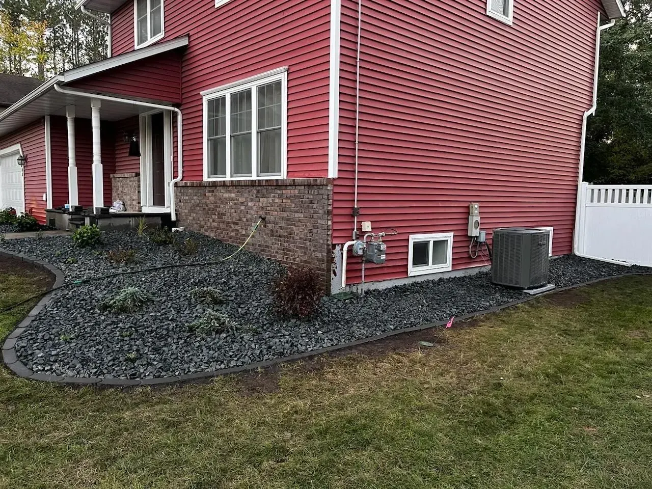 Red-sided house with a black stone landscape bed and green grass lawn.  The bed is bordered by dark gray edging.