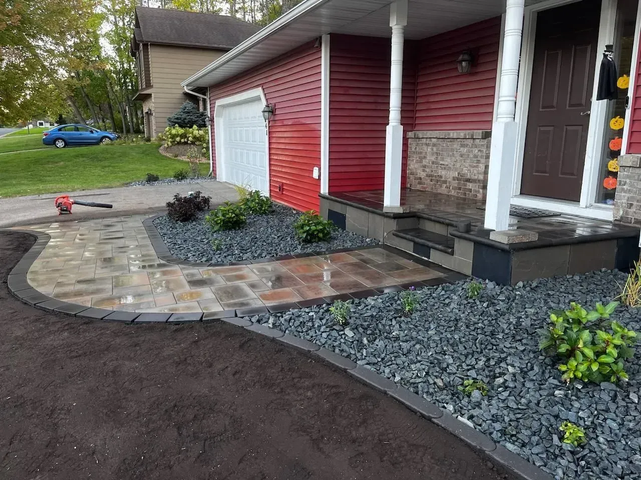 A home with a red exterior and a newly paved walkway leading to the front door, bordered by dark grey rocks and plants.