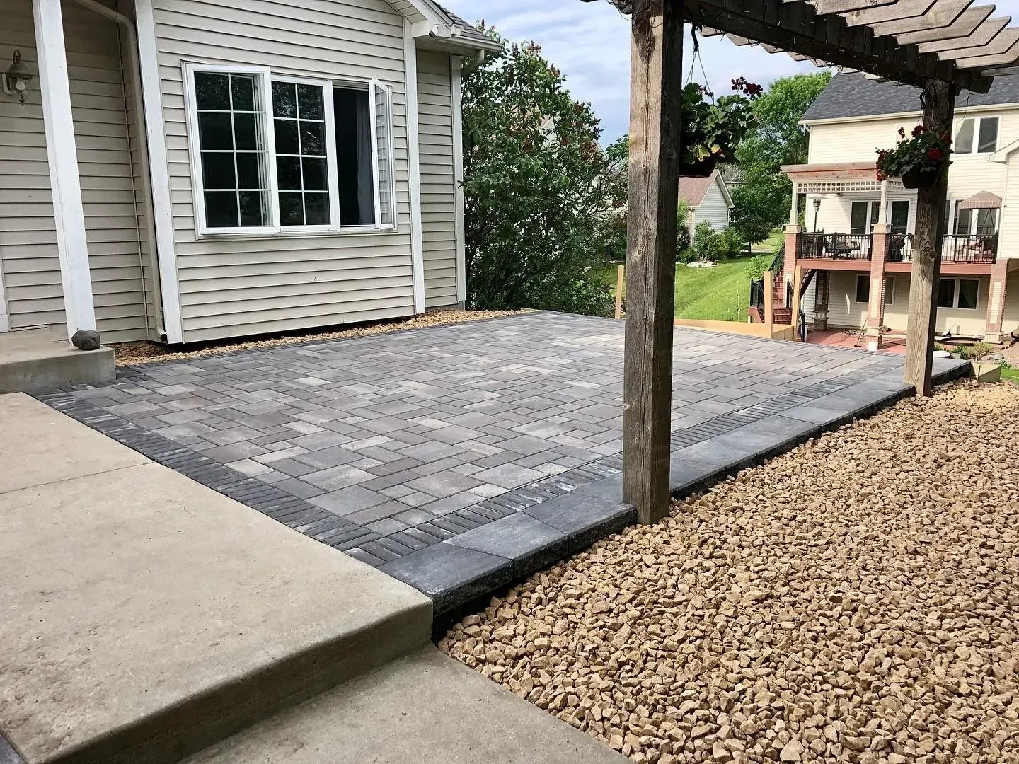 Brick patio next to a house with a pergola. Brown gravel borders the patio's side.