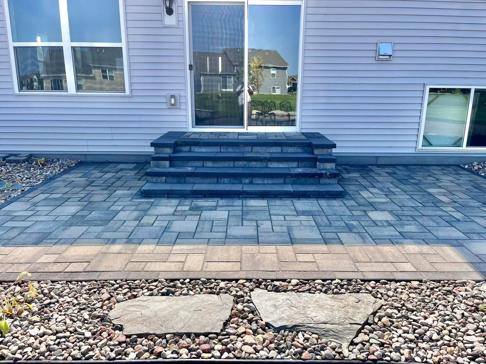 Stone walkway leading from a porch, bordered by dark pavers and gravel, alongside newly seeded grass.