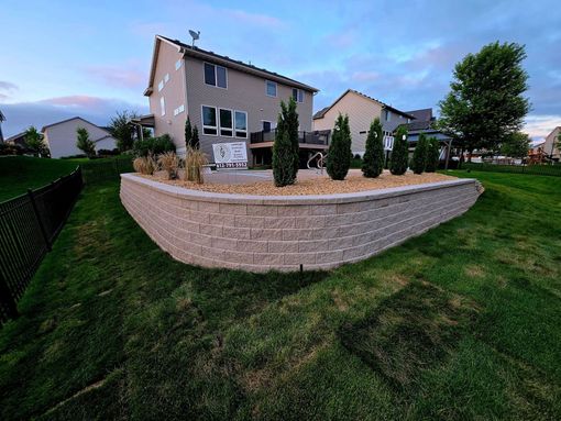 A gravel bed with a few dormant plants next to a house and driveway. The corner is lined with black edging.