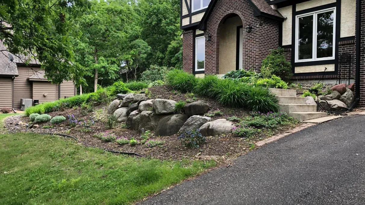 Exterior of a house with a brick facade and a landscaped front yard featuring large rocks and various green plants.