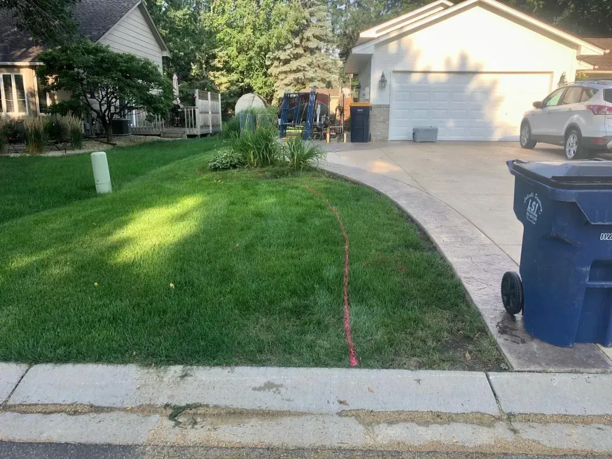 Lawn with a curved sidewalk, grass, and a trash bin in a suburban setting, a red line marking the lawn.