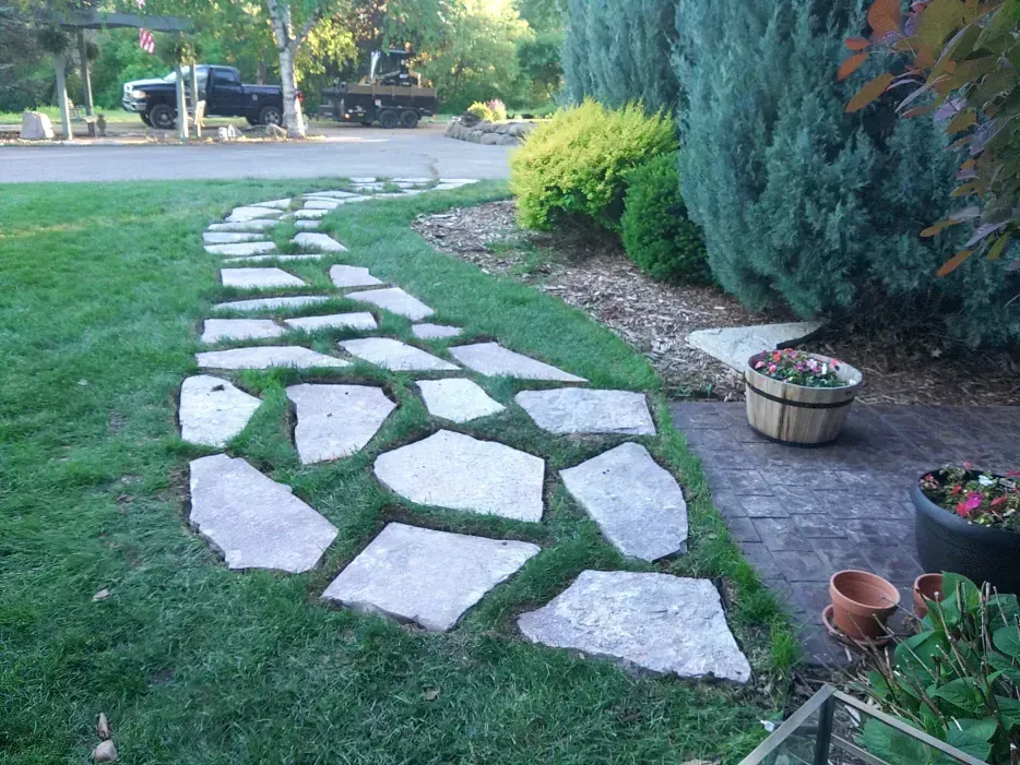Stone path winding through green grass, leading toward a driveway and garden.