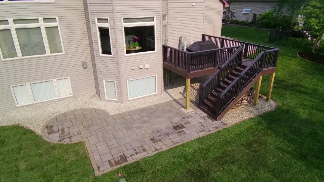 Backyard with a wooden deck, patio, and green lawn. House has beige siding and windows.