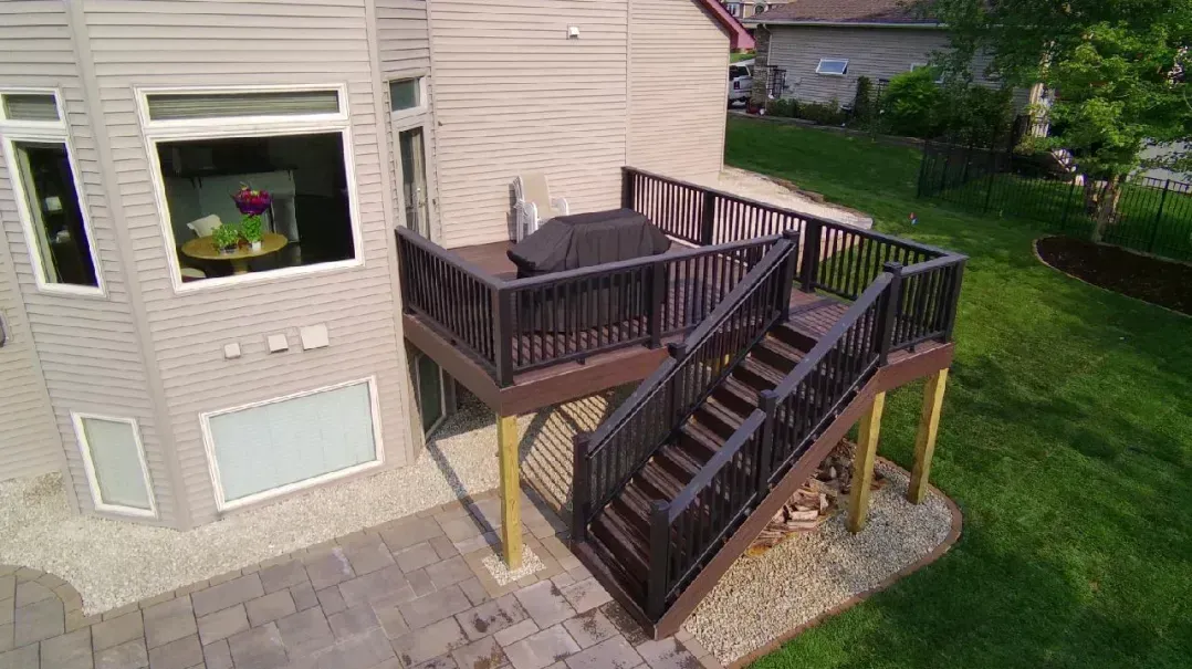 Elevated wooden deck with stairs, dark railings, and a grill