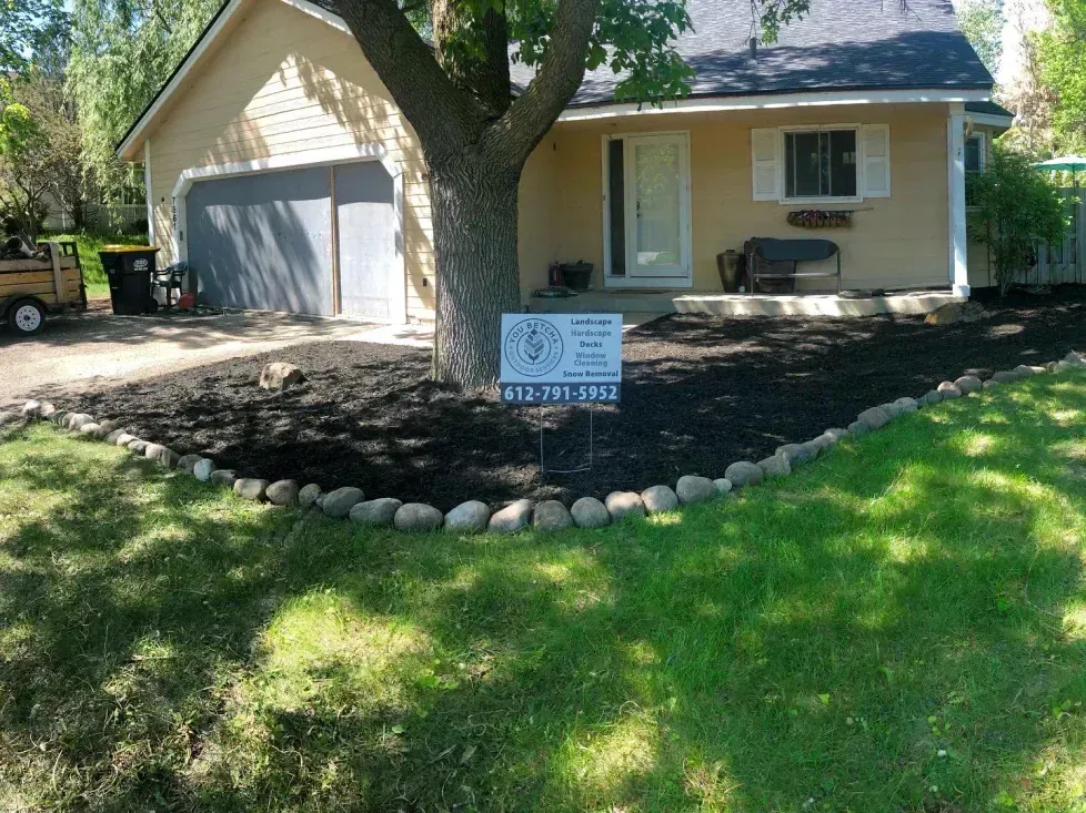 A house with a new mulch bed around a tree in the front yard. The lawn is green, and the mulch is dark.