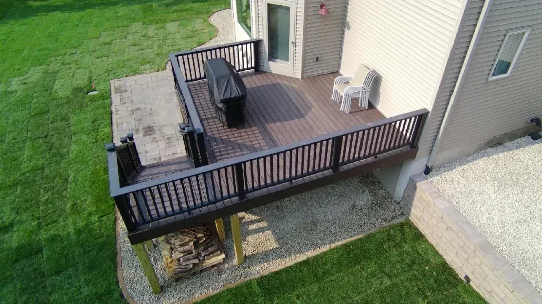Aerial view of a composite deck with brown railing and grilling area, adjacent to a beige house. 