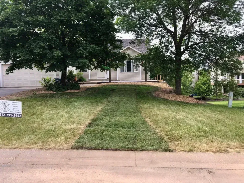 A house with a sloping front yard. A strip of green grass leads up to the home; surrounding lawn is brown.