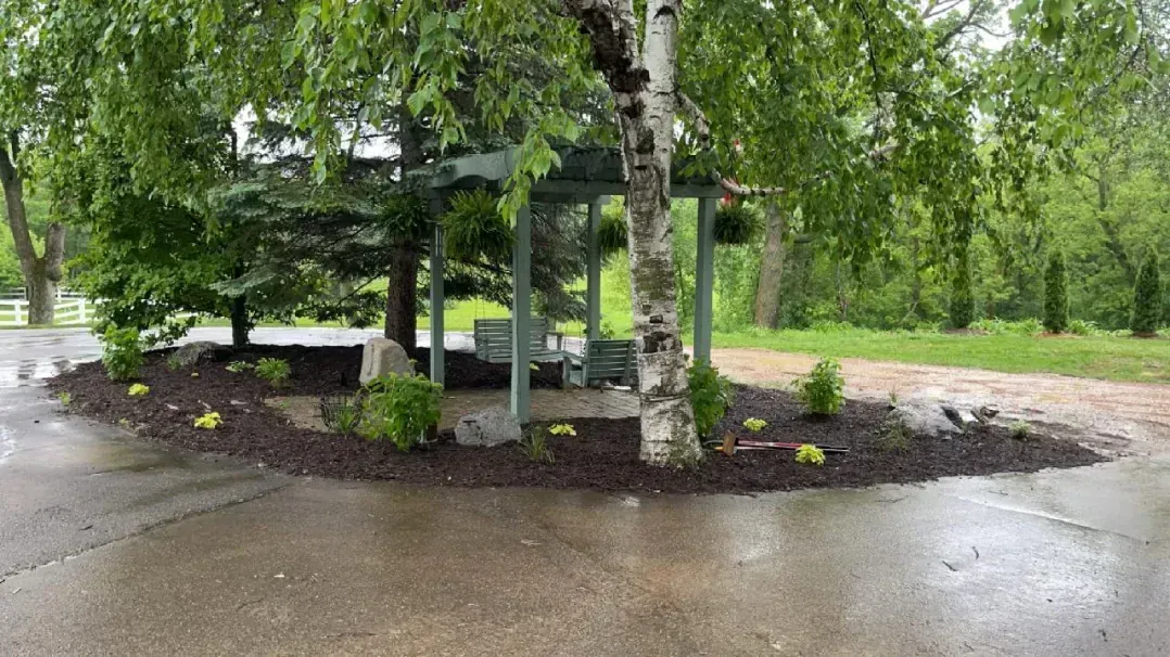 A small gazebo surrounded by trees and landscaping, on a rainy day.