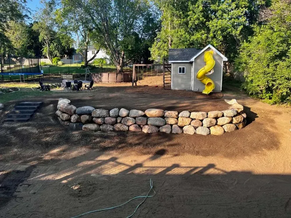 Backyard playground with a rock wall, playhouse with a yellow slide, and a swing set. 