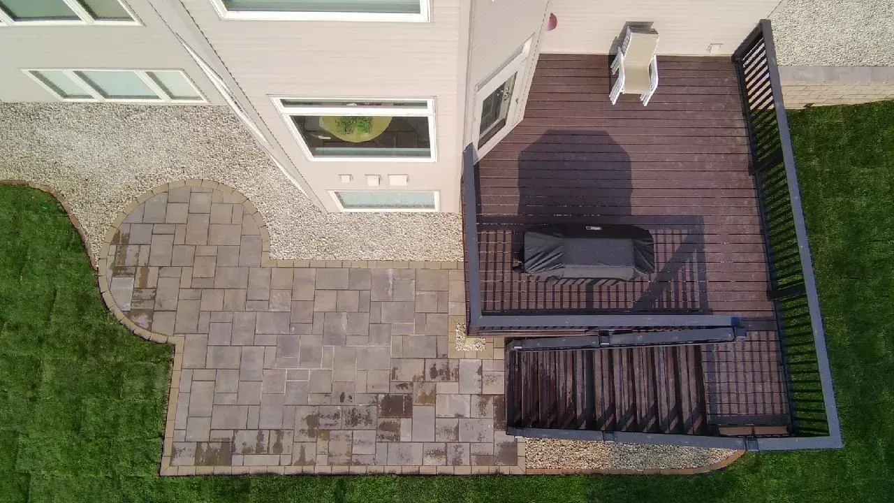 Overhead view of a house with a dark wood deck, a stone patio, and a grassy yard. A grill sits on the deck.
