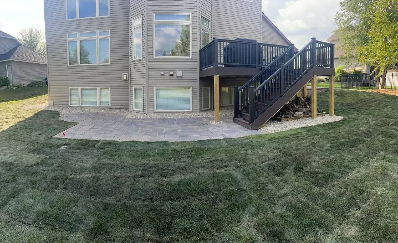 Backyard with a house featuring a deck and stairs, a stone patio, and a sloped lawn.